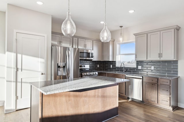 kitchen with tasteful backsplash, a kitchen island, pendant lighting, stainless steel appliances, and light stone countertops