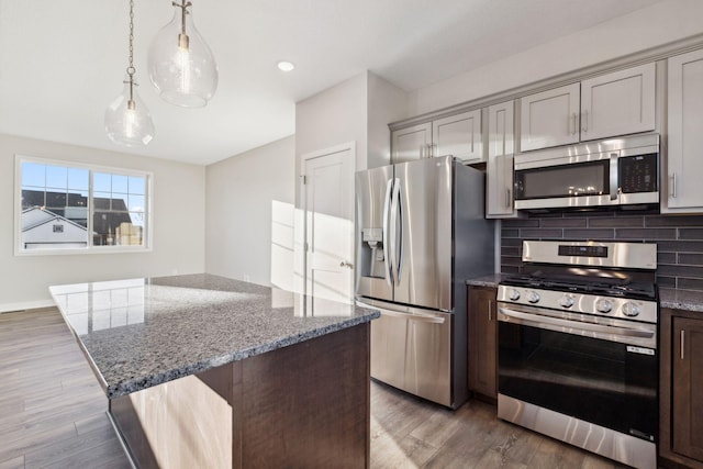 kitchen with stone countertops, hardwood / wood-style floors, decorative light fixtures, and appliances with stainless steel finishes