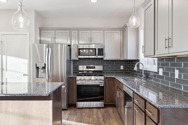 kitchen featuring stainless steel appliances, stone countertops, sink, and hanging light fixtures