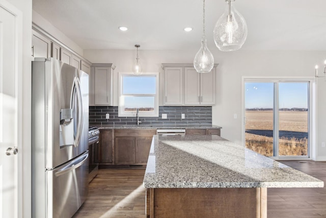 kitchen featuring stainless steel refrigerator with ice dispenser, light stone counters, hanging light fixtures, a kitchen island, and decorative backsplash