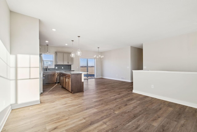 kitchen with tasteful backsplash, wood-type flooring, hanging light fixtures, a kitchen island, and a notable chandelier