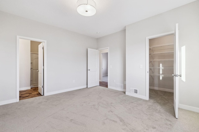 unfurnished bedroom with light carpet, a spacious closet, a closet, and ensuite bathroom