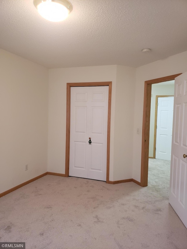 unfurnished bedroom with light carpet, a textured ceiling, and a closet