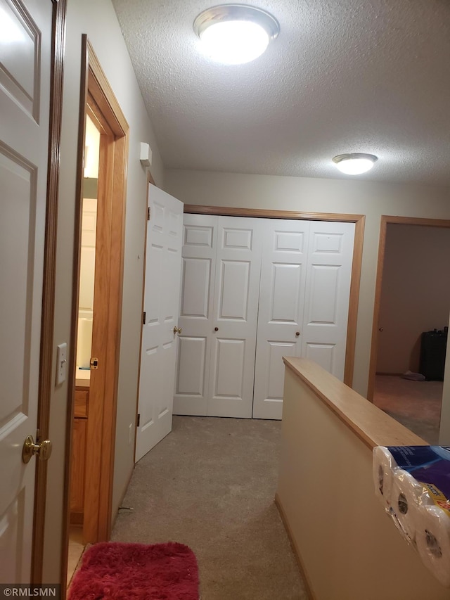 corridor with a textured ceiling and light colored carpet