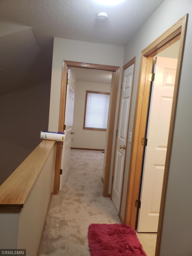 hallway featuring light colored carpet and a textured ceiling