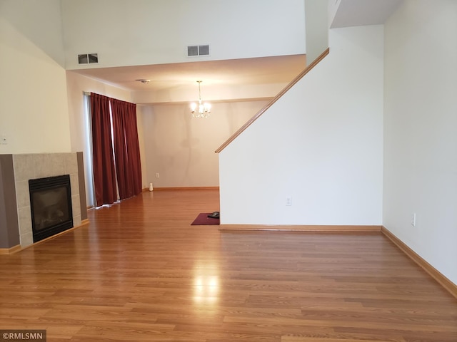 unfurnished living room featuring a tile fireplace, hardwood / wood-style floors, a towering ceiling, and a notable chandelier