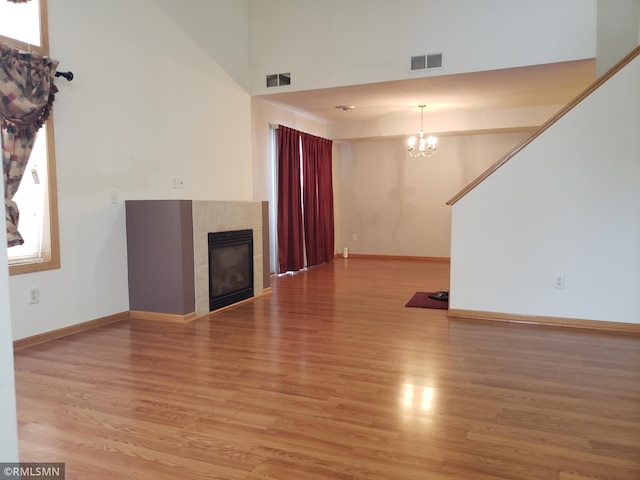 unfurnished living room with a chandelier, light wood-type flooring, a towering ceiling, and a tiled fireplace