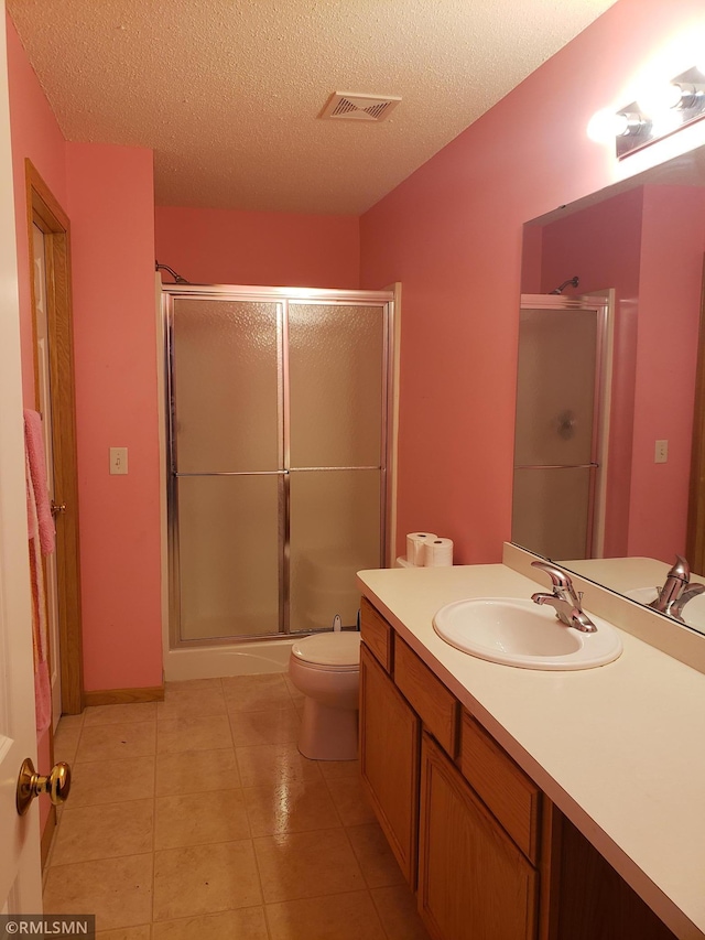 bathroom with tile patterned floors, vanity, a textured ceiling, toilet, and a shower with shower door