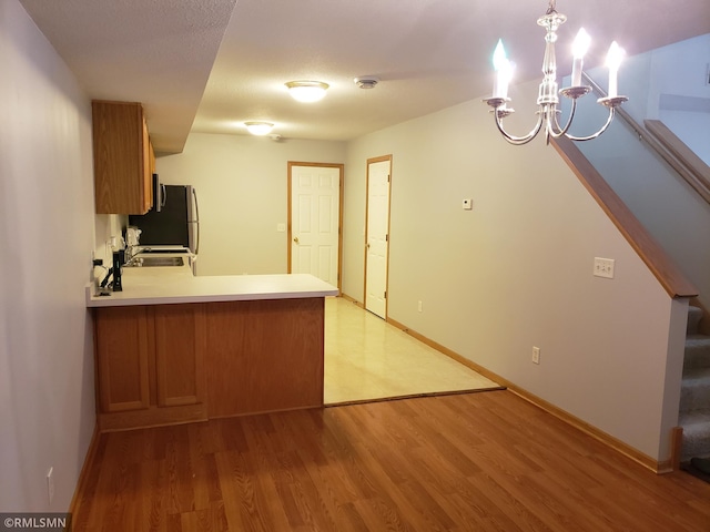 kitchen with decorative light fixtures, stainless steel fridge, a notable chandelier, kitchen peninsula, and light hardwood / wood-style flooring