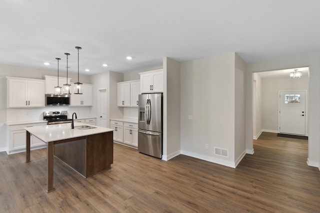 kitchen with appliances with stainless steel finishes, a kitchen island with sink, sink, dark hardwood / wood-style floors, and hanging light fixtures