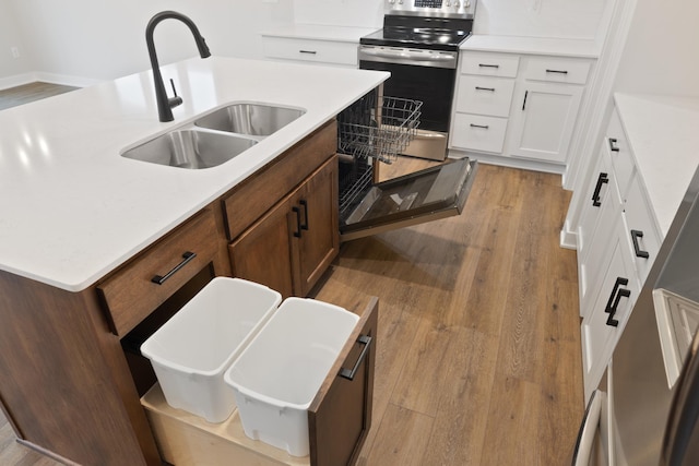 kitchen with white cabinets, stainless steel range oven, sink, and light hardwood / wood-style flooring