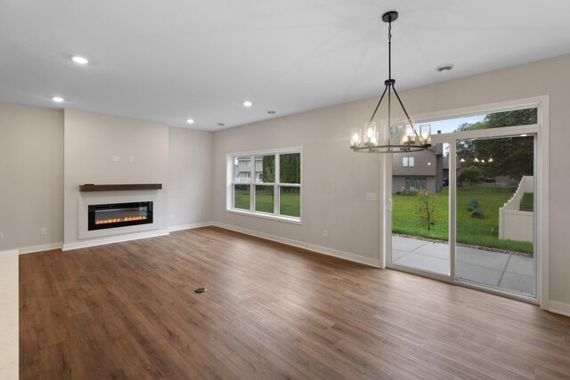 unfurnished living room featuring a healthy amount of sunlight, wood-type flooring, and an inviting chandelier