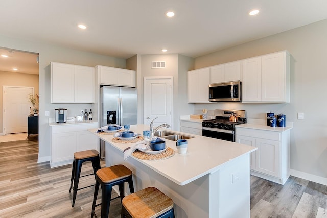 kitchen featuring a center island with sink, sink, appliances with stainless steel finishes, light hardwood / wood-style floors, and white cabinetry