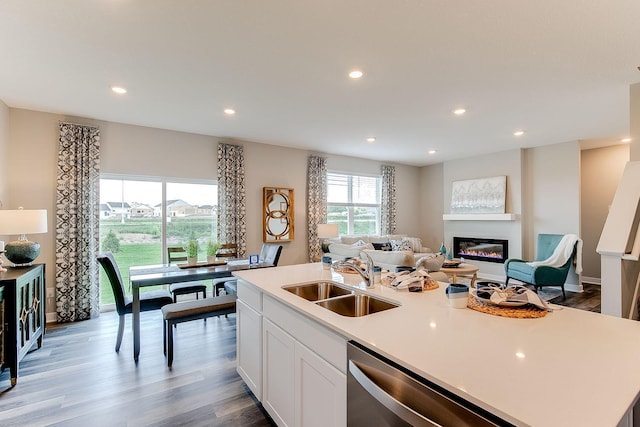 kitchen with stainless steel dishwasher, sink, a center island with sink, light hardwood / wood-style flooring, and white cabinets