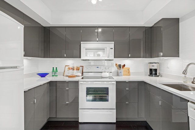 kitchen with white appliances, decorative backsplash, a sink, and gray cabinetry