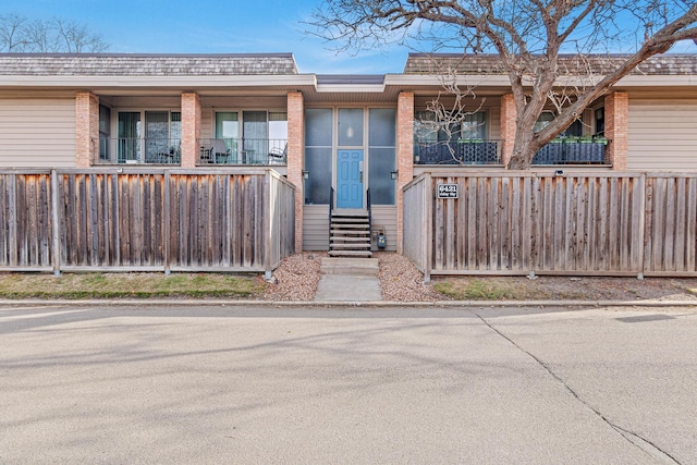 property entrance with roof with shingles, fence, brick siding, and mansard roof