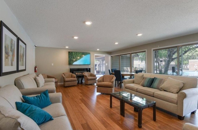 living area with a textured ceiling, light wood-type flooring, a glass covered fireplace, and recessed lighting