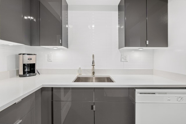 kitchen featuring tasteful backsplash, gray cabinets, light countertops, white dishwasher, and a sink