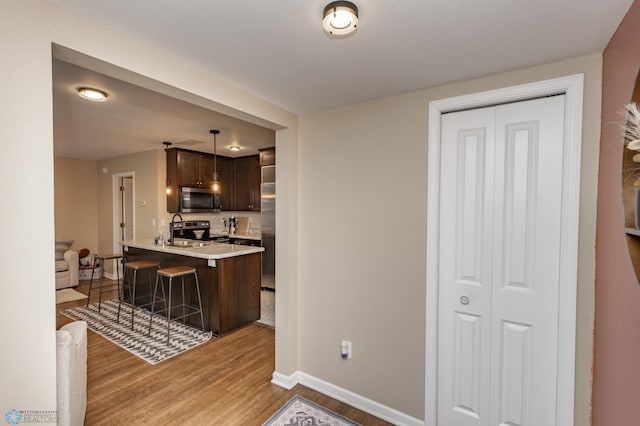 kitchen with a kitchen breakfast bar, decorative light fixtures, dark brown cabinets, light hardwood / wood-style floors, and stainless steel appliances