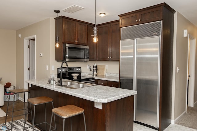 kitchen with dark brown cabinetry, stainless steel appliances, sink, pendant lighting, and a breakfast bar area