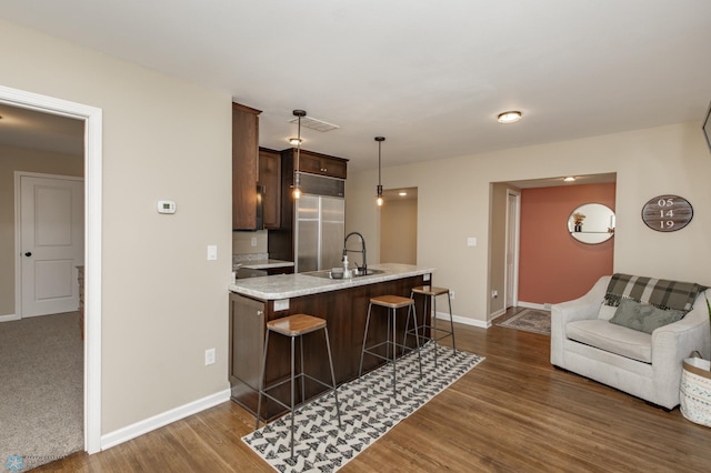 kitchen with dark brown cabinetry, sink, dark hardwood / wood-style floors, hanging light fixtures, and a breakfast bar area