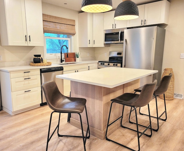 kitchen with a kitchen breakfast bar, light wood-type flooring, a kitchen island, white cabinetry, and stainless steel appliances