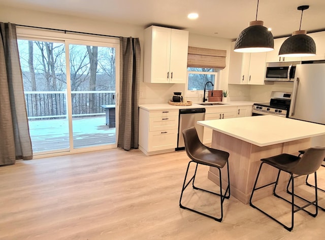 kitchen with light wood-type flooring, stainless steel appliances, sink, decorative light fixtures, and white cabinets