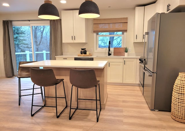 kitchen featuring a wealth of natural light, light hardwood / wood-style flooring, hanging light fixtures, and appliances with stainless steel finishes