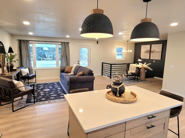 kitchen with a textured ceiling, a kitchen island, hanging light fixtures, and light hardwood / wood-style flooring