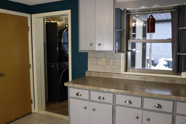 kitchen with white cabinetry, stacked washer / drying machine, light tile patterned floors, and backsplash