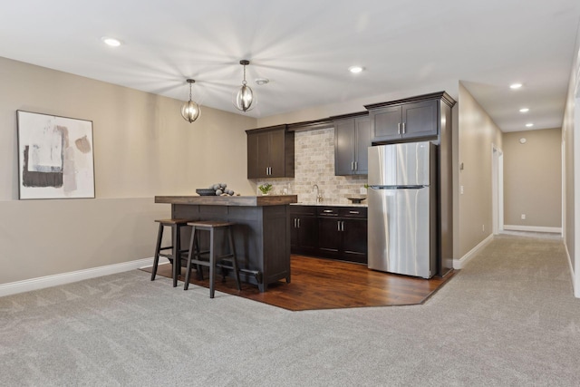 kitchen featuring dark brown cabinets, freestanding refrigerator, dark carpet, a kitchen bar, and pendant lighting