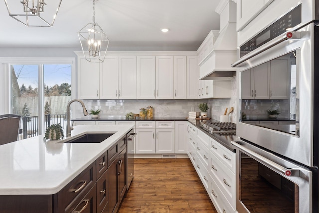 kitchen with pendant lighting, custom exhaust hood, light countertops, appliances with stainless steel finishes, and a sink