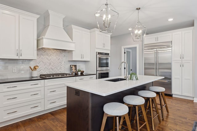 kitchen featuring stainless steel appliances, dark countertops, custom range hood, and a sink