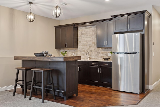 kitchen with dark brown cabinetry, hanging light fixtures, backsplash, freestanding refrigerator, and a kitchen bar