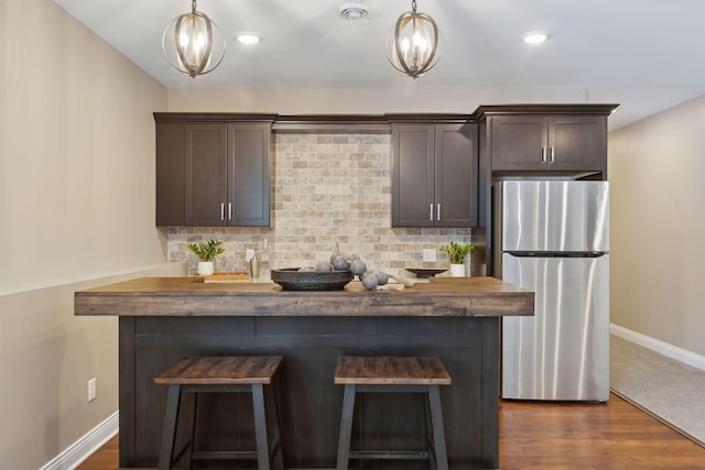 kitchen featuring baseboards, dark brown cabinets, backsplash, freestanding refrigerator, and decorative light fixtures