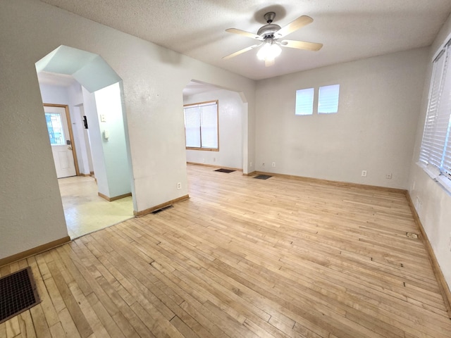 empty room with ceiling fan, light wood-type flooring, and a textured ceiling