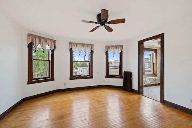 unfurnished room with radiator, a wealth of natural light, ceiling fan, and light wood-type flooring