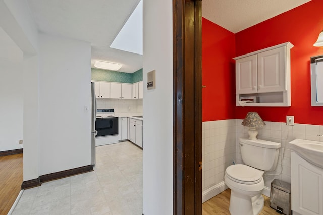 bathroom featuring vanity, baseboards, a wainscoted wall, tile walls, and toilet