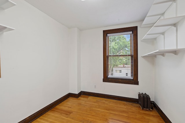 spare room featuring radiator heating unit, light wood-type flooring, and baseboards