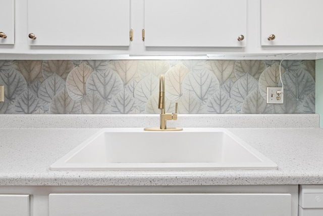 interior details with white cabinetry, sink, backsplash, and light stone counters