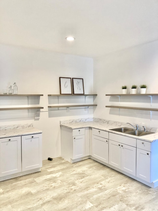 kitchen with light stone countertops, sink, white cabinets, and light hardwood / wood-style flooring