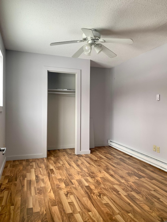 unfurnished bedroom featuring a textured ceiling, ceiling fan, a baseboard heating unit, and hardwood / wood-style flooring