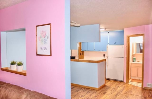 kitchen featuring kitchen peninsula, a textured ceiling, white fridge, and blue cabinets