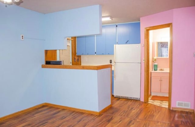 kitchen featuring white fridge, kitchen peninsula, and blue cabinetry