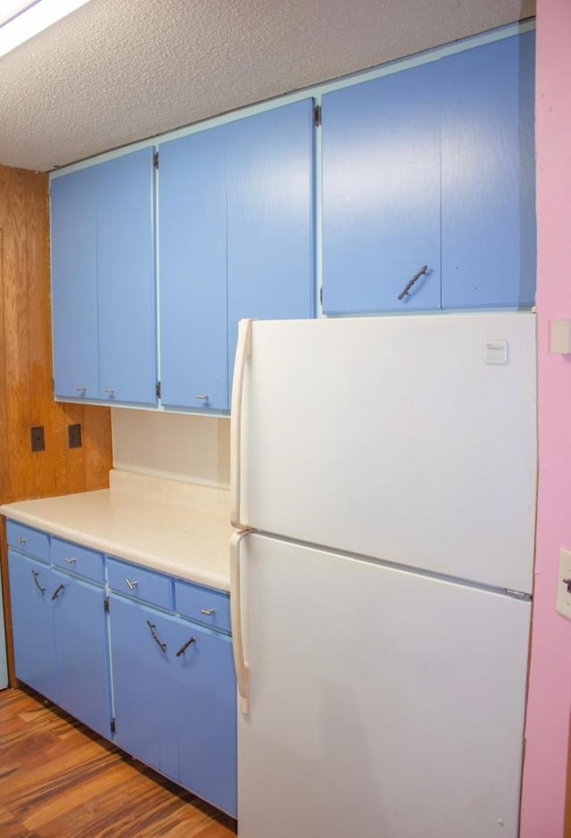 kitchen with a textured ceiling, white fridge, dark hardwood / wood-style flooring, and blue cabinetry