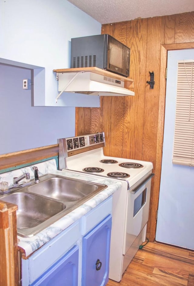 kitchen with wood walls, white range with electric cooktop, sink, light wood-type flooring, and a textured ceiling