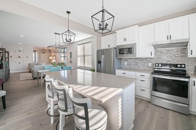 kitchen featuring decorative light fixtures, white cabinetry, a kitchen island, and appliances with stainless steel finishes