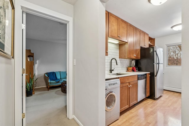 kitchen with backsplash, sink, light hardwood / wood-style flooring, stainless steel appliances, and washer / clothes dryer