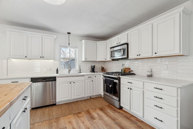 kitchen featuring appliances with stainless steel finishes, sink, pendant lighting, white cabinets, and light hardwood / wood-style floors