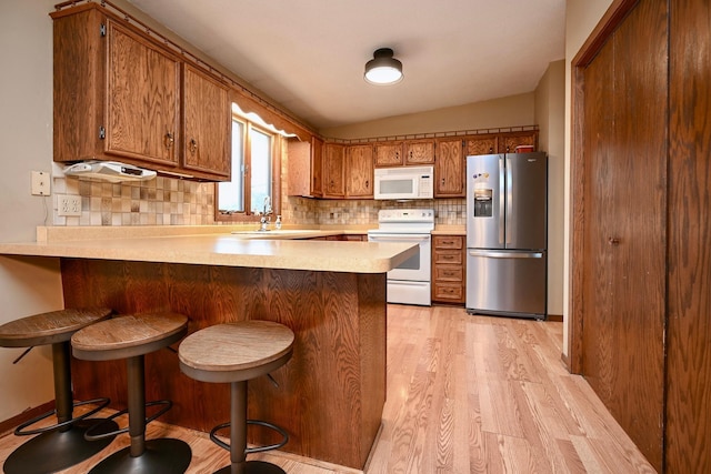 kitchen with a breakfast bar, white appliances, sink, light hardwood / wood-style floors, and kitchen peninsula